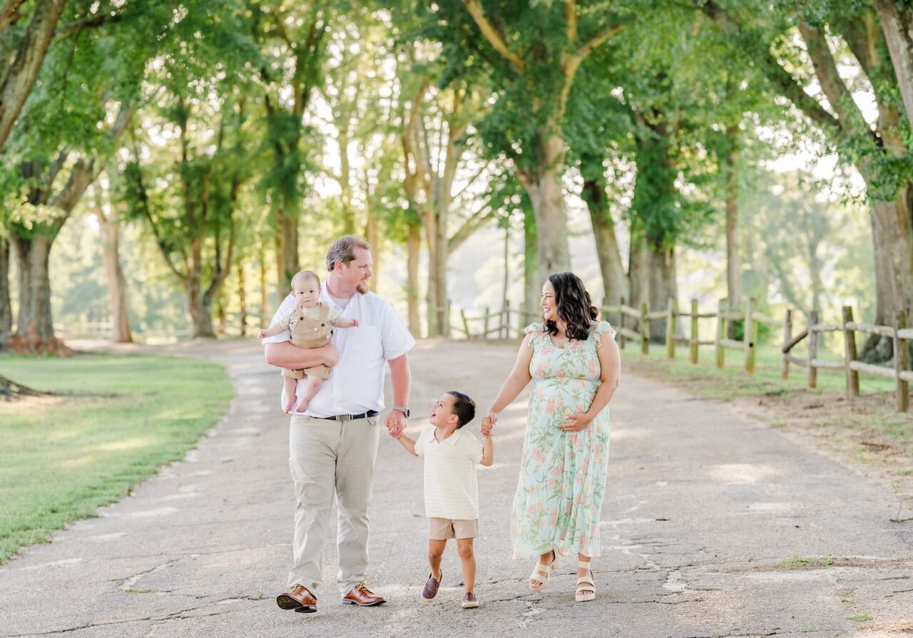 A lively moment on a family walk. The young boy laughs happily as he holds hands with his parents, looking up at his father who smiles back down at him.